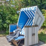Weiße Strandkorb mit blau-weißem Stoff und dunkler Decke im Garten.