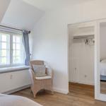 Schlafzimmer mit Dachschräge, Fenster, Stuhl und Blick in die Garderobe.