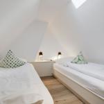 Zwei Einzelbetten in einem Dachzimmer mit weißen Wänden und Holzboden.