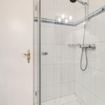 Duschkabine mit Glaswand und Duschbrause. Weiße Fliesen und Heizkörper sichtbar.