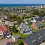 Aerial view of a coastal village with houses, roads, and the sea in the background.