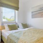 Bedroom with bed, nightstand, and window. Wall art shows beach.