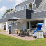 Terrace with table, chairs, and beach chairs in front of a house with balcony.