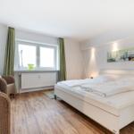 Bedroom with white bed, wooden floor, and window with green curtains.