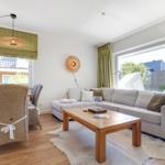 Living and dining area with sofa, table and chairs. Large windows and green curtains.
