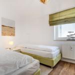 Two beds with white linens, window with green roller blind and wall art.