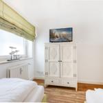 Room with two beds, white wardrobe, and TV. Window with roller blind and floor heating.