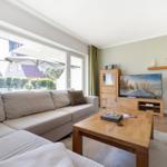 Living room with sofa, wooden table, and TV. Access to garden with umbrella.