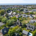 Aerial view of a coastal town with houses, greenery, and the sea in the background.