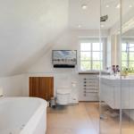 Duschbereich mit Glaswand, Badewanne, Toilette und TV an der Wand.