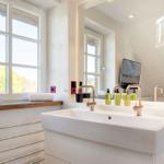 Badezimmer mit Waschbecken, Spiegel und Fenster mit Blick auf Grün.