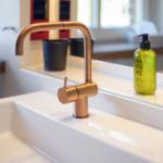 Waschbecken mit Kupferhahn und grünen Pflegeprodukten