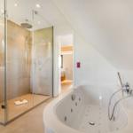 Dusche mit Glaswand und Badewanne mit Massagefunktion.