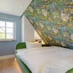 Schlafzimmer mit grünem Bett und buntem Tapetenwand