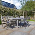 Terrasse mit Tisch und Stühlen, umgeben von Hecke und Grünflächen.