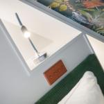 Bettkopfteil mit grünem Stoff, Lampe und Wandbehang mit Tiermotiven.
