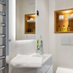 Badezimmer mit Waschbecken, Spiegel und eingebauter Holzregalwand mit Pflegeprodukten.