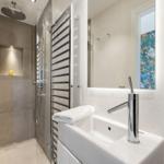 Moderne Dusche mit Regenduschkopf und Handtuchhalter. Waschbecken mit Spiegel und grüne Steckdose.
