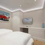 Schlafzimmer mit Bett, Fernseher und Wandbild. Holzboden und weiße Möbel.