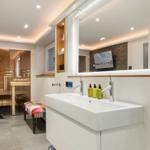 Bad mit Dusche, Waschbecken und Sauna im Hintergrund.