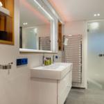 Badezimmer mit Waschbecken, Spiegel, Dusche und Heizkörper.