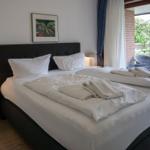 Doppelbett mit weißen Bettwäsche und Handtüchern. Fensterblick auf Balkon und Grünfläche.