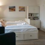 Schlafzimmer mit weißem Bett, Nachttisch, Wandbildern und Stauraum.