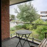 Terrasse mit Tisch und Bank. Blick auf Grünflächen und Gebäude.