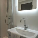 Bad mit Dusche, Waschbecken und beleuchtetem Spiegel.
