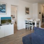 Wohn- und Essbereich mit Küchenbereich, blauer Sofa und Fernseher auf weißem Schrank.
