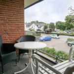 Terrasse mit Tisch und Stühlen, Blick auf Straße und Grünflächen.