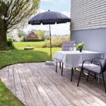 Terrace with table, chairs, and umbrella next to house wall