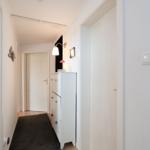 Hallway with white doors, cabinet, and wall lamp. Dark rug on the floor.