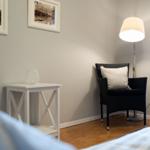 Black chair with pillow, floor lamp, and table with candle against wall with pictures.