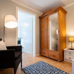 Bedroom with wooden wardrobe, bed, nightstand, and armchair.
