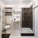 Bathroom with shower, sink, and toilet. White tiles and dark accents.