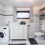 Bathroom with washing machine, sink, toilet, and window with curtains.