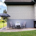 Terrace with table, two chairs, and umbrella in front of white brick wall.