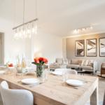 Dining room with wooden table and chairs. Living area with sofa and wall pictures in background.