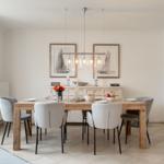 Dining room with wooden table, chairs, and wall art. Ceiling light and window visible.