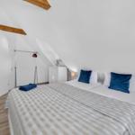 Schlafzimmer mit Dachschräge, Bett mit blauen Kissen und Holzbalken an der Decke.