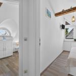 Schlafzimmer mit Bett, Fenster und Holzdecke. Nebenraum mit Schrank und Bogenfenster.