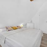 Schlafzimmer mit Dachschräge, weißem Bett und Holzboden. Zwei Nachttische mit Lampen.