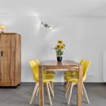 Esszimmer mit Holztisch, vier gelben Stühlen und einem Holzschrank. An der Wand hängt ein Anker.