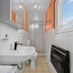 Badezimmer mit Waschbecken, Toilette und Dusche. Fenster und Wandverkleidung.