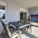 Terrasse mit Tisch, Stühlen und Strandkorb. Fenster und Glastür führen ins Haus.