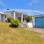 Wohnhaus mit Garage, Terrasse und Garten unter blauem Himmel.