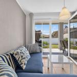 Ein Wohnzimmer mit Sofa, Tisch und Terrasse. Durchgehende Glastüren führen auf die Terrasse.