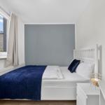 Schlafzimmer mit weißem Bett, blauer Decke und Fenster mit Blick auf Dach.