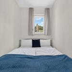 Ein Schlafzimmer mit einem Bett, blauer Decke und Fenster mit Blick auf Grün.